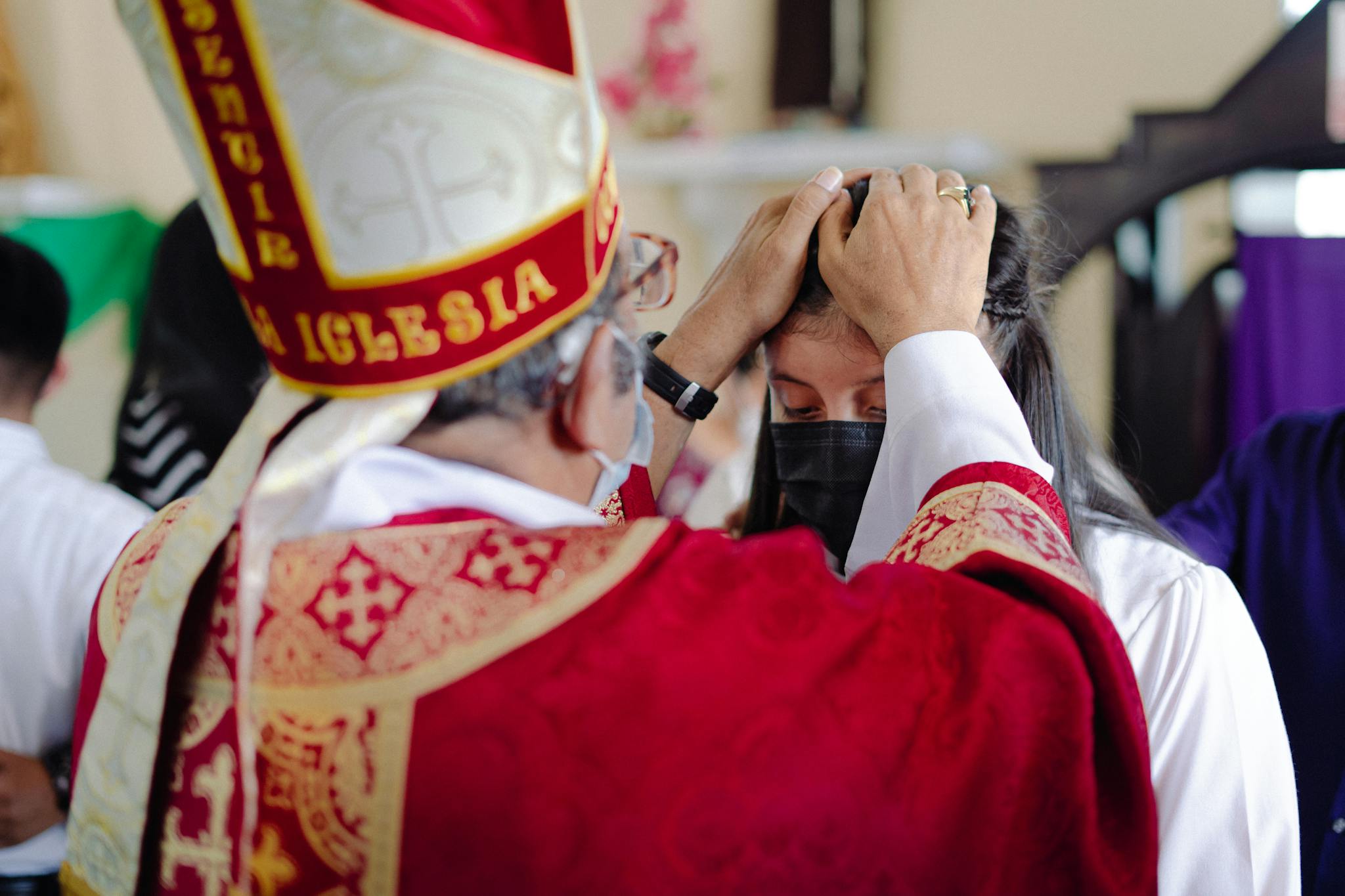Bishop blessing a participant during a traditional religious service inside a church setting.