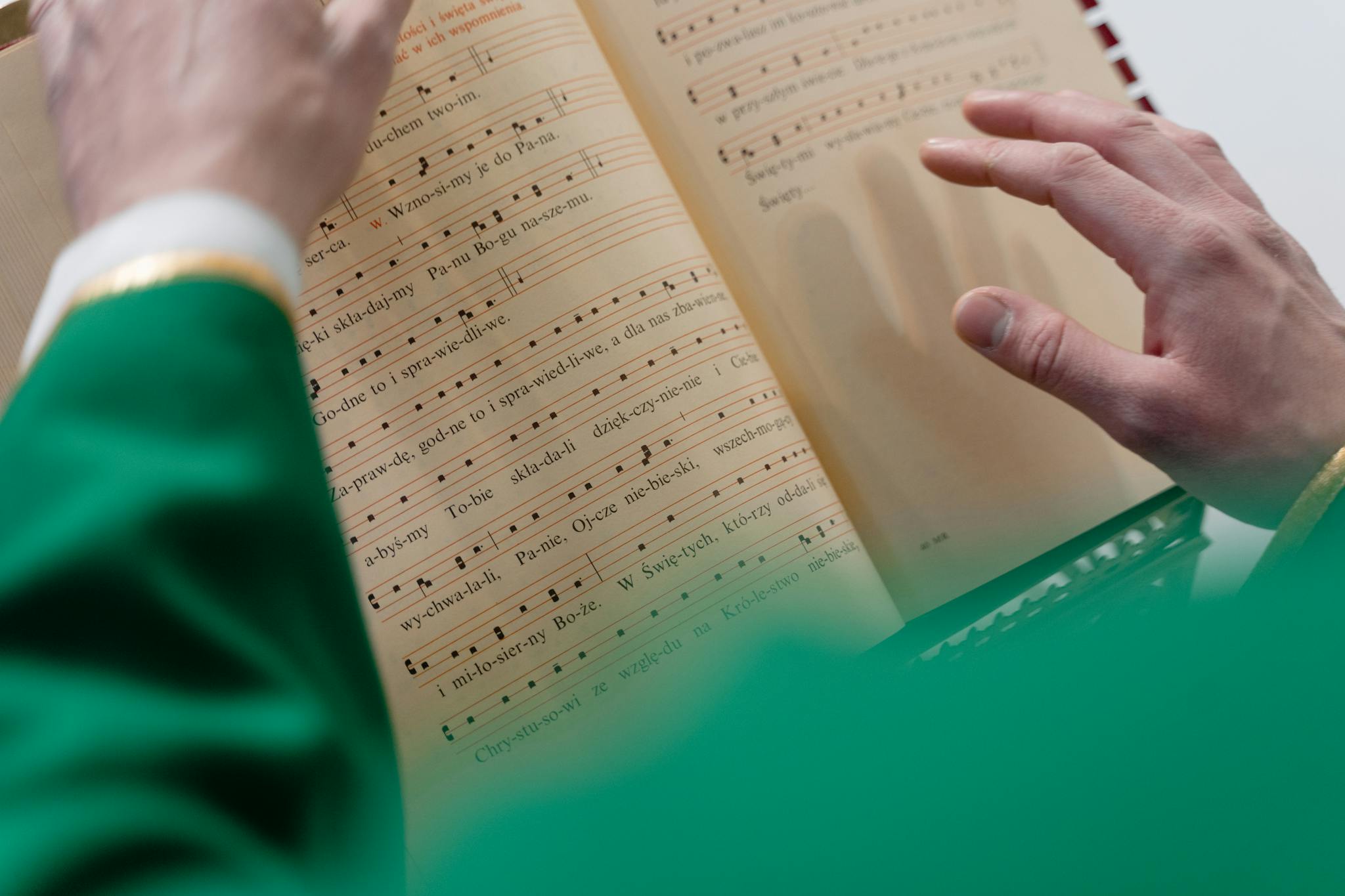 Close-up of a priest in green robes reading religious sheet music, highlighting the spirituality aspect.